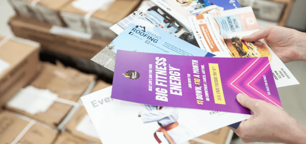A person holding a stack of colorful flyers in their hands.